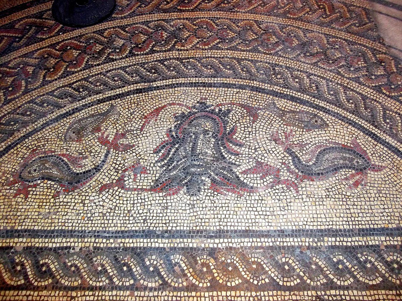 Tête d’une divinité marine dans une mosaïque romaine de Fordington, généralement identifiée comme Océanos ; le registre patrimonial admet aussi Neptune. Dorset Museum, Angleterre. Témoin romain postérieur aux épopées homériques
